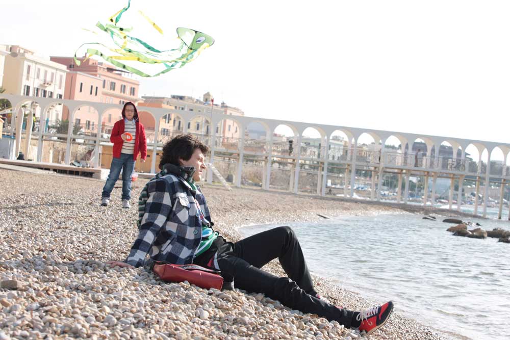 Matteo (Andrea Bosca) guarda pensieroso il mare mentre un bimbo, dietro di lui, si diverte a far volare il suo aquilone. -  Dall'articolo: Vestiti da Febbre da fieno.